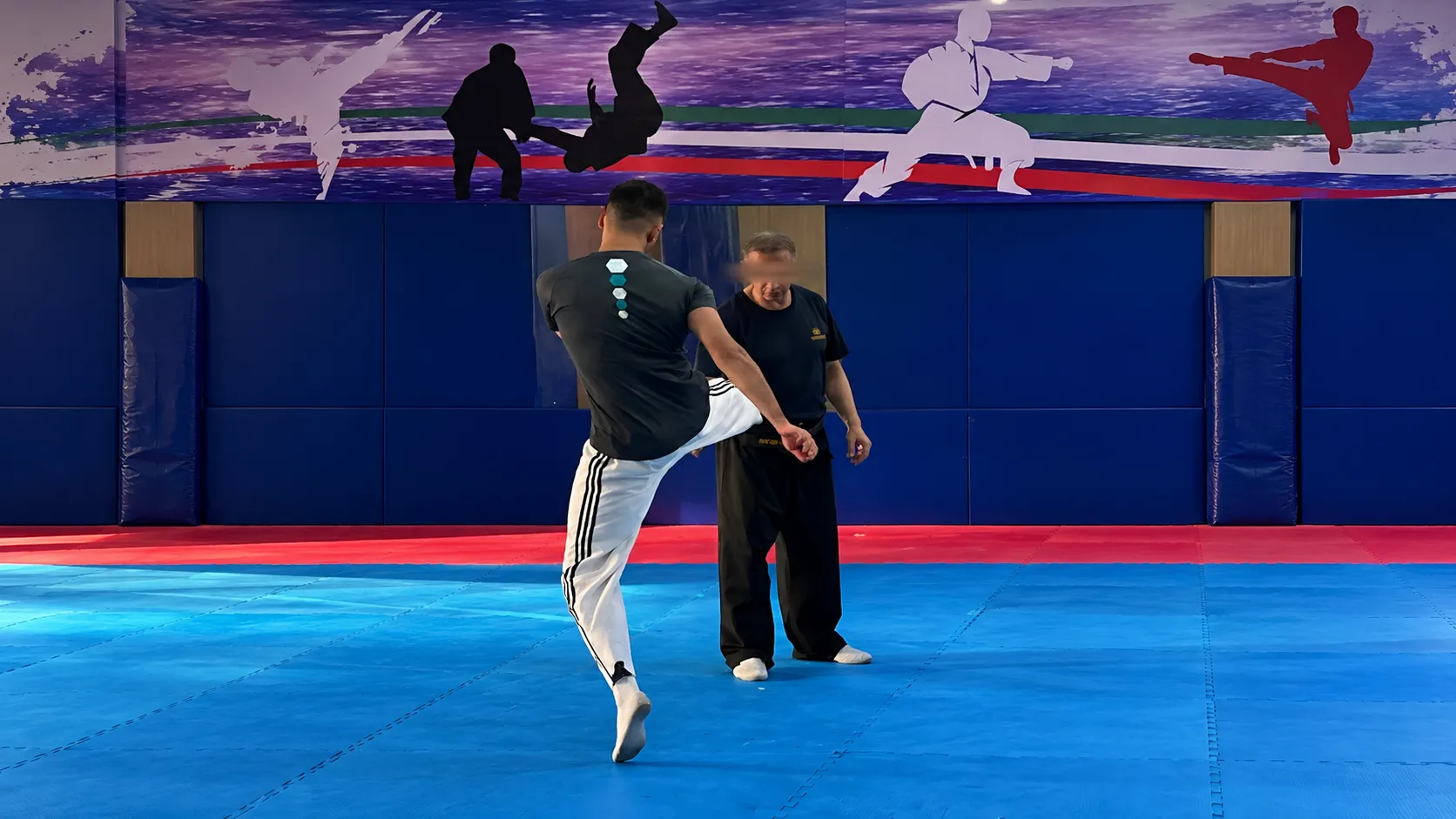Me practising a kick with a training partner on blue taekwondo mats